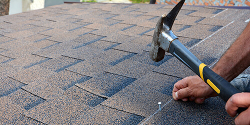 Roofer hammering a nail into a shingle.